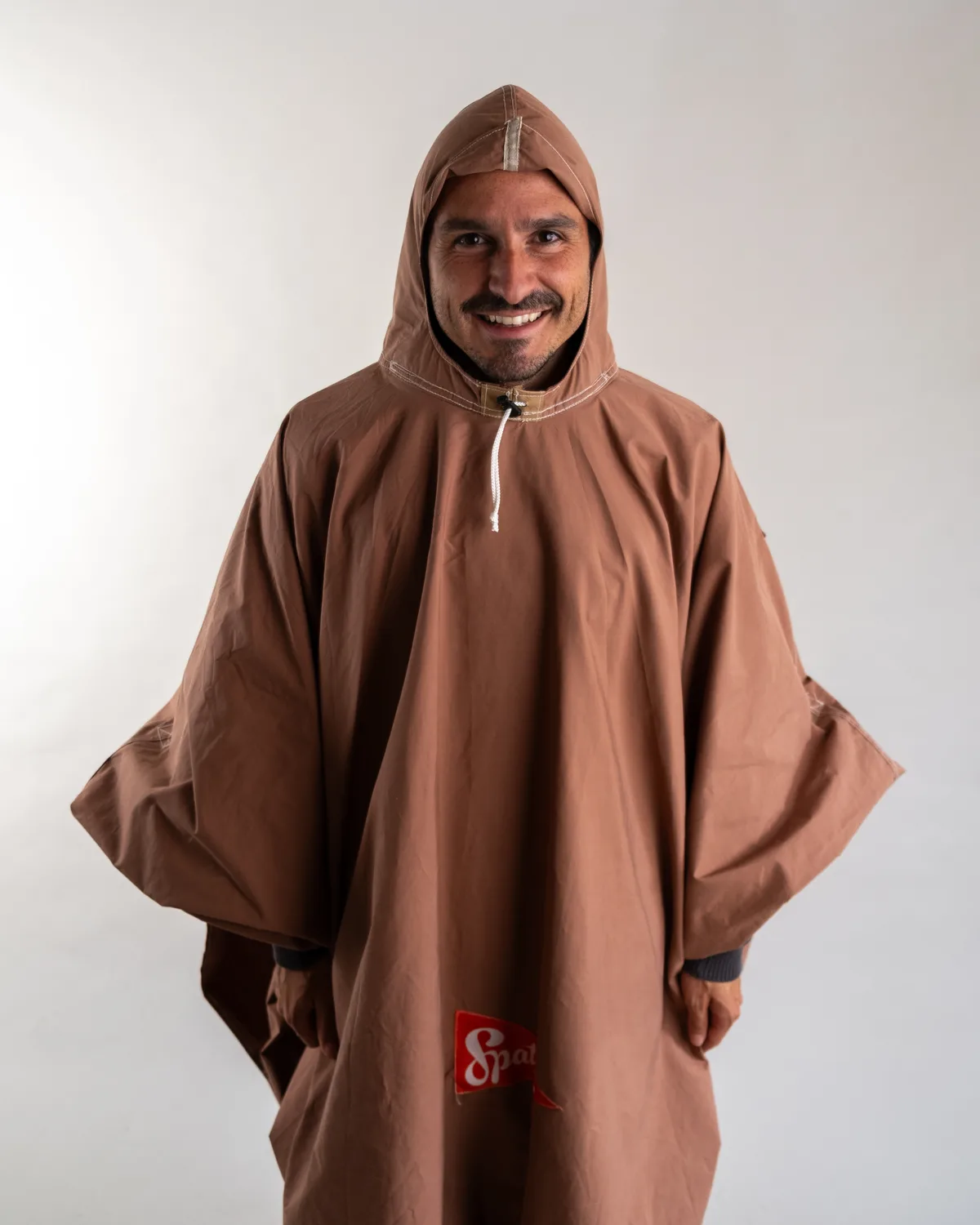 Ein grinsender Mann in einem rostbraunen Poncho.